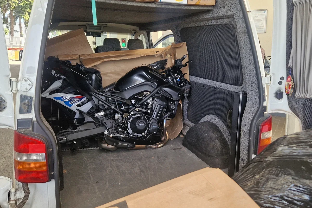 Czarny motocykl sportowy przewożony wewnątrz białego furgonu dostawczego, widziany z otwartych drzwi bagażnika.