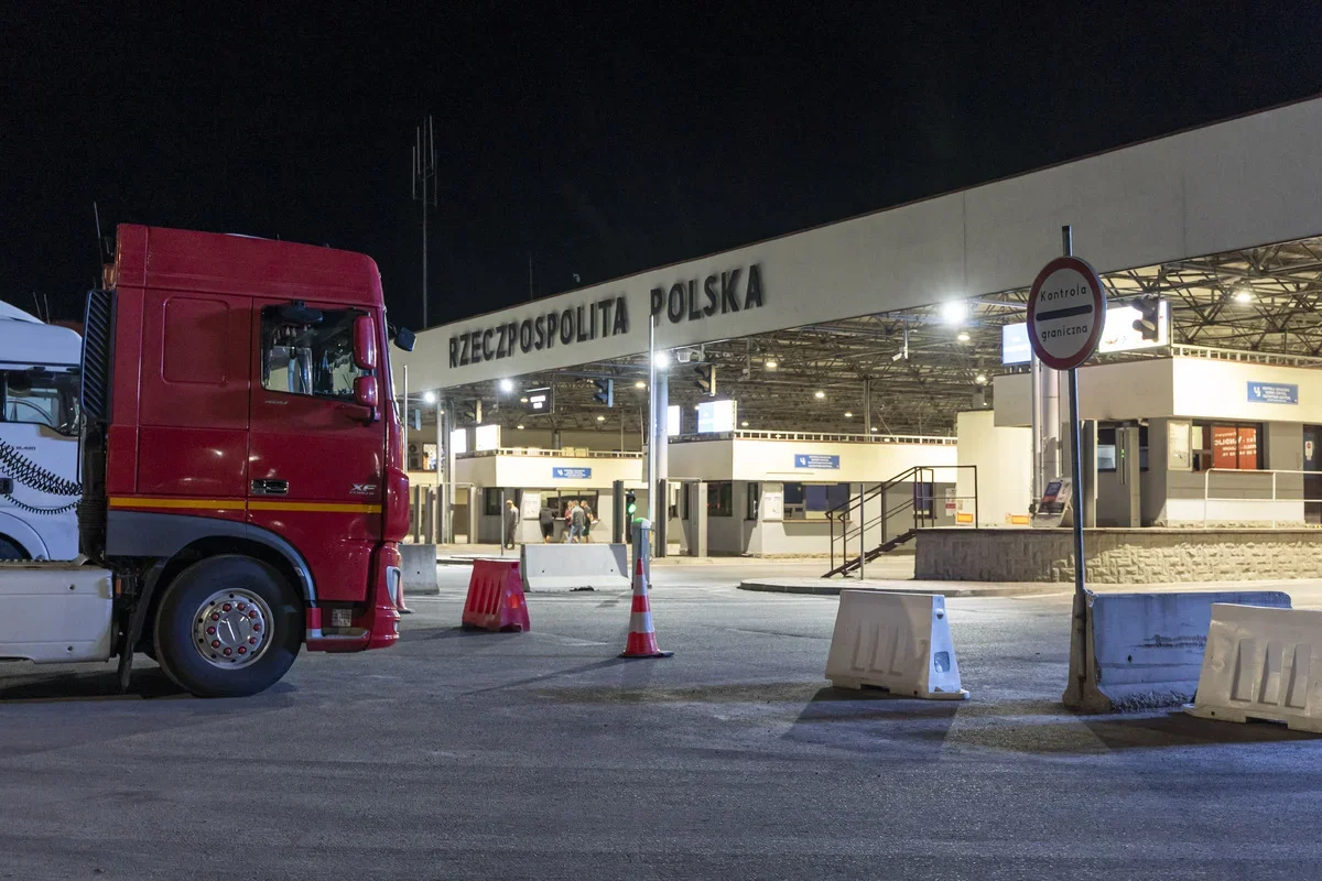 Czerwona ciężarówka stoi przed nocną polską strefą kontroli granicznej.