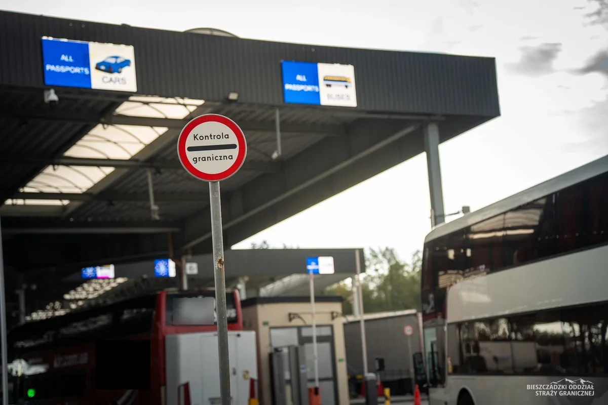 Przejście graniczne z zatłoczonymi pasami dla samochodów i autobusów, na pierwszym planie znak „Kontrola graniczna”.