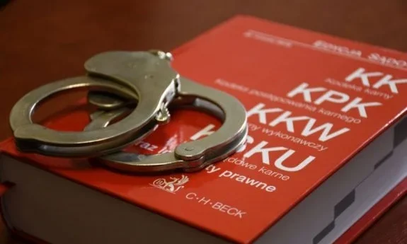 Metalowe kajdanki leżące na czerwonej okładce książki z kodeksami karnymi wydawnictwa C.H.Beck.