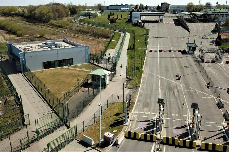 Pusty przejazd graniczny z budynkami kontroli, szlabanami i ogrodzeniami w słoneczny dzień.