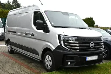 Srebrny furgon Nissan Interstar zaparkowany na brukowanym parkingu w ciągu dnia.