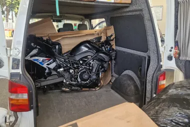 Czarny motocykl sportowy przewożony wewnątrz białego furgonu dostawczego, widziany z otwartych drzwi bagażnika.