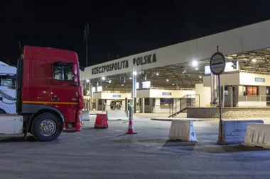 Czerwona ciężarówka stoi przed nocną polską strefą kontroli granicznej.